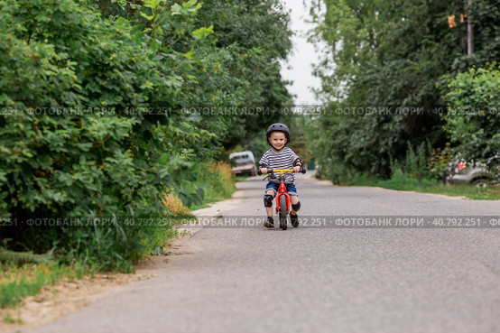 A cheerful little boy rides a running bike in a helmet outdoors. A happy child is engaged in an active sport. Protection. Life insurance and child safety. Стоковое фото, фотограф Photojuli / Фотобанк Лори