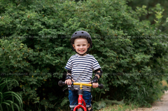 A cheerful little boy rides a running bike in a helmet outdoors. A happy child is engaged in an active sport. Protection. Life insurance and child safety. Стоковое фото, фотограф Photojuli / Фотобанк Лори