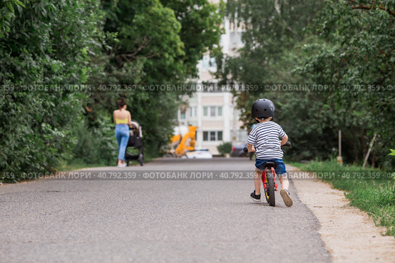 A cheerful little boy rides a running bike in a helmet outdoors. A happy child is engaged in an active sport. Protection. Life insurance and child safety. Стоковое фото, фотограф Photojuli / Фотобанк Лори