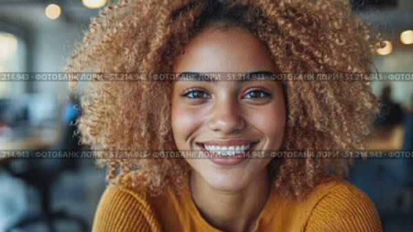 A cheerful woman with vibrant curly hair beams while sitting in an inviting office space filled with natural light. Стоковое AI-видео, аниматор Данила Большаков / Фотобанк Лори