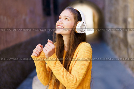 A cheerful young woman with stylish headphones beams with happiness, enjoying her favorite music in a charming alleyway. Her vibrant outfit and joyful expression radiate pure love for music. A Joyful Young Woman Enthusiastically Listening to Music While Strolling in a Scenic Alley. Стоковое фото, агентство Ingram Publishing / Фотобанк Лори