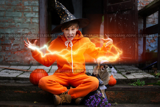 A child in an orange costume and a wizard hat for Halloween. The boy holds the skeleton and conjures a magical magical lightning bolt. Стоковое фото, фотограф Лазаренко Светлана / Фотобанк Лори