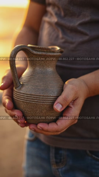 A child's small hands holding a clay water jug, symbolizing the thirst of Imam Hussain family, under the fading light of sunset. Стоковое AI-видео, аниматор Sergey Grishin / Фотобанк Лори