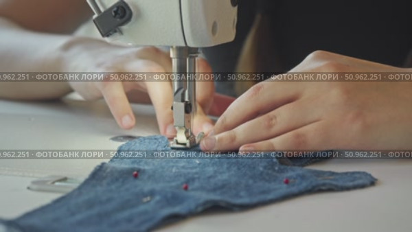 A close-up shot of a seamstress's hands working with sewing machines on a piece of denim fabric, which is pierced with pins. Стоковое видео, видеограф Strunov David / Фотобанк Лори
