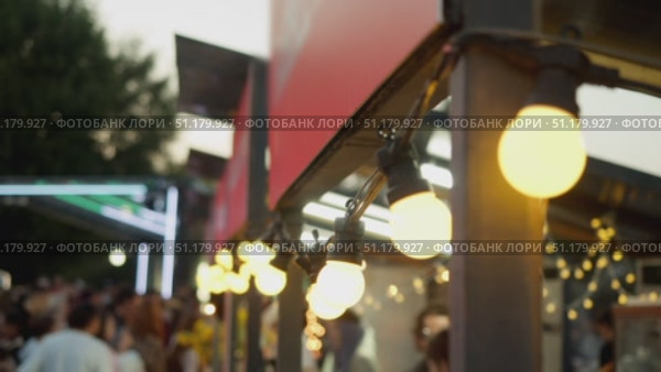 A close-up shot of lanterns, burning with warm yellow light and hanging from a market kiosk at a street food festival. Стоковое видео, видеограф Strunov David / Фотобанк Лори