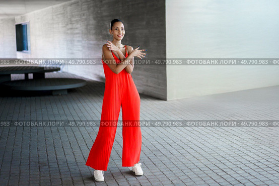 A confident woman poses in a vibrant red jumpsuit that reflects her unique style, against a stunning architectural background, showcasing a blend of modern fashion and timeless elegance. A Stylish Woman in a Red Jumpsuit Posing Confidently Outdoors with an Air of Elegance. Стоковое фото, агентство Ingram Publishing / Фотобанк Лори