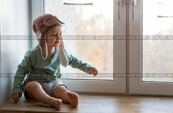 A cute 2-year-old boy in a cap is playing on the windowsill with a wooden airplane. Children's wooden toys for child development. Стоковое фото, фотограф Photojuli / Фотобанк Лори