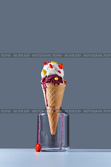 A delicious dessert in a waffle cone with red and yellow pills and lollipops stands in a glass jar on gray background. The concept of summer catarrhal diseases and their treatment with place for text.. The waffle cone stands in glass jar with a ball of berry and vanilla ice cream with red and yellow pills and a lollipops on a dark gray background. Copy space. Стоковое фото, агентство Ingram Publishing / Фотобанк Лори