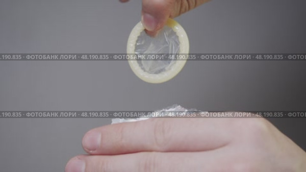 A detailed view of a man's hands, removing a condom from its packaging prior to sexual activity, against a white backdrop. Стоковое видео, видеограф Strunov David / Фотобанк Лори