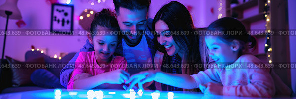 A family gathers around a table playing with glowing toys, enjoying quality time together in a warmly decorated space during the evening. Стоковое AI-изображение, AI-художник Данила Большаков / Фотобанк Лори