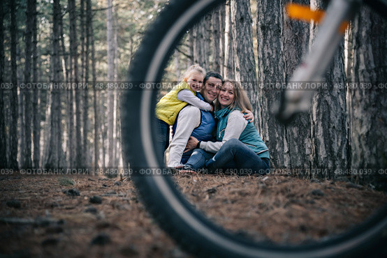 A family rides bicycles through the forest. A creative perspective through a bicycle wheel. Стоковое фото, фотограф София Тюленева / Фотобанк Лори