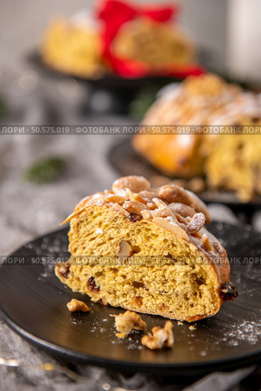 A generous slice of Bolo Rainha, a traditional Portuguese Christmas cake, is presented on a dark plate. Topped with almonds and powdered sugar, it showcases a rich, fruit-studded interior. Стоковое фото, агентство Ingram Publishing / Фотобанк Лори