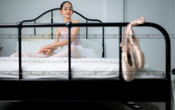 A girl ballet student warm up in bed and look at the old ballet shoes hanging from the end of the bed. Стоковое фото, агентство Ingram Publishing / Фотобанк Лори