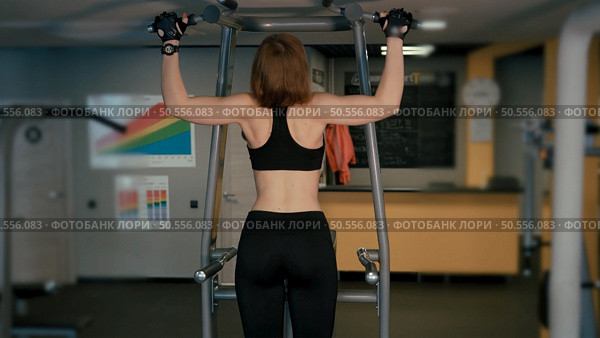 A girl training with a simulator sitting her back to the camera. Training for back muscles. Стоковое фото, агентство Ingram Publishing / Фотобанк Лори