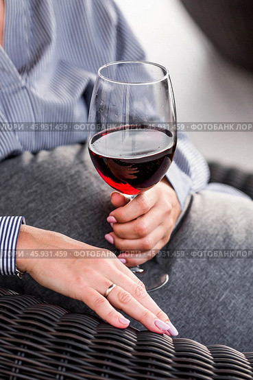 A glass of red alcoholic drink or wine in a woman's hand. A woman is resting on the veranda of a country house. The concept of relaxation, party or celebration. Стоковое фото, фотограф Photojuli / Фотобанк Лори