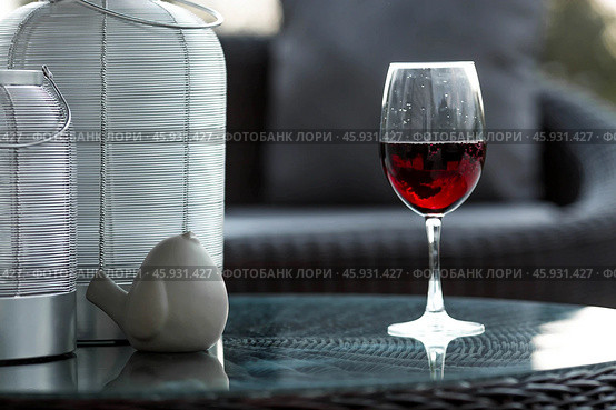 A glass of red alcoholic drink or wine on a glass table on the veranda. The concept of alcoholism, a party, or a holiday. Стоковое фото, фотограф Photojuli / Фотобанк Лори