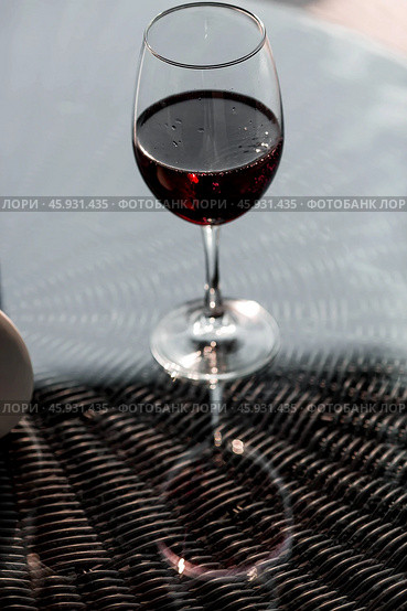 A glass of red alcoholic drink or wine on a glass table on the veranda. The concept of alcoholism, a party, or a holiday. Стоковое фото, фотограф Photojuli / Фотобанк Лори