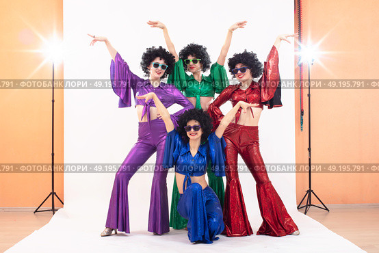 A group of girls in colorful flared suits and afro wigs pose in a photo studio. Disco style from the eighties or seventies. Стоковое фото, фотограф Лазаренко Светлана / Фотобанк Лори