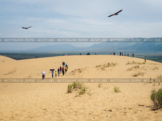 A group of tourists enjoy the views after climbing a sand dune (2021 год). Редакционное фото, фотограф Саблин Станислав / Фотобанк Лори
