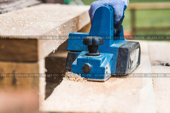 A hand-held electric planer in the hands of a craftsman. A man planing boards with an electric tool. Production of wooden products. Construction, wood processing. Стоковое фото, фотограф Photojuli / Фотобанк Лори