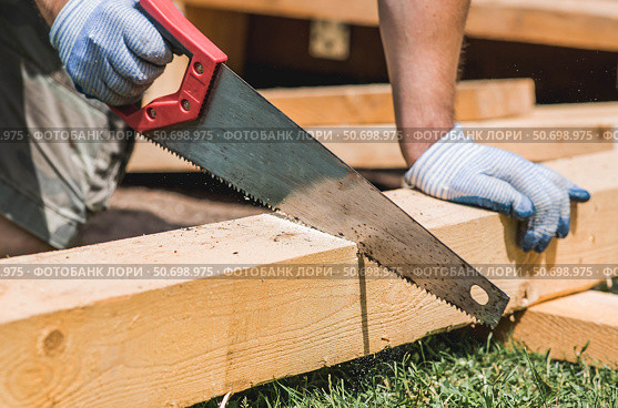 A hand saw in the hands of a craftsman. A man sawing a beam with a tool. Production of wooden products. Construction, wood processing. Стоковое фото, фотограф Photojuli / Фотобанк Лори