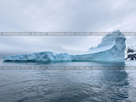A huge high breakaway glacier drifts in the southern ocean off the coast of Antarctica at sunset, the Antarctic Peninsula, the Southern Arctic Circle, azure water, cloudy weather. Стоковое фото, фотограф Vladimir Drozdin / Фотобанк Лори