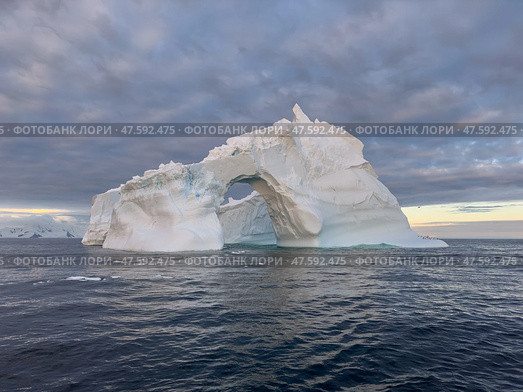 A huge high breakaway glacier drifts in the southern ocean off the coast of Antarctica at sunset, the Antarctic Peninsula, the Southern Arctic Circle, azure water, cloudy weather. Стоковое фото, фотограф Vladimir Drozdin / Фотобанк Лори