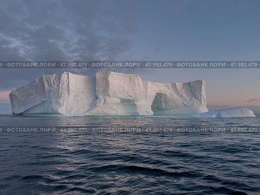 A huge high breakaway glacier drifts in the southern ocean off the coast of Antarctica at sunset, the Antarctic Peninsula, the Southern Arctic Circle, azure water, cloudy weather. Стоковое фото, фотограф Vladimir Drozdin / Фотобанк Лори