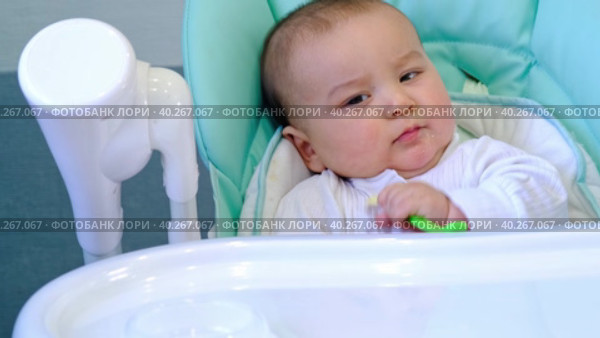 A hungry baby is gnawing on a plastic spoon at the table on a high chair. Teething, whims, itchy gums, introduction of complementary foods. Стоковое видео, видеограф Ольга Симонова / Фотобанк Лори