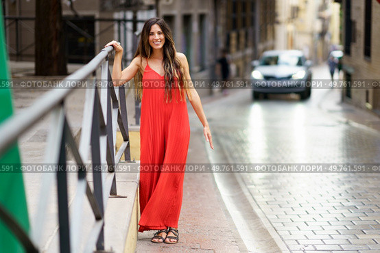 A joyful woman in a stylish red dress walks confidently down a charming street, radiating elegance against a captivating urban backdrop, enchanting and bringing smiles to those around her. A charming woman in a vibrant red dress strolls gracefully through a scenic European street. Стоковое фото, агентство Ingram Publishing / Фотобанк Лори