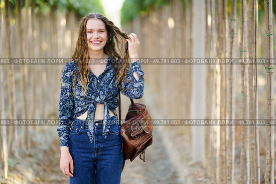 A joyful young woman stands gracefully among lush greenery, dressed in a stylish outfit and beaming with a radiant smile, embodying happiness and confidence for lifestyle and fashion themes. A Charming Young Woman Embracing Nature while Sporting a Stylish and Fashionable Outfit. Стоковое фото, агентство Ingram Publishing / Фотобанк Лори