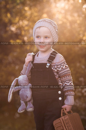 A little boy of 4 years old outdoors with a suitcase and a stuffed rabbit goes on a journey. A beautiful portrait of a child playing on the street. Стоковое фото, фотограф Photojuli / Фотобанк Лори