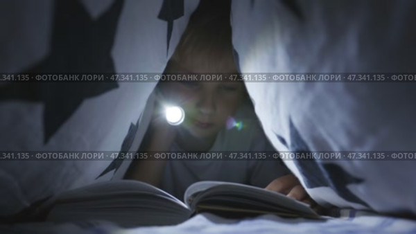 A little boy reads a book with a flashlight under the covers at night. Стоковое видео, видеограф Mikhail Davidovich / Фотобанк Лори