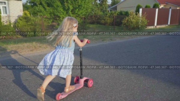 A little girl in the village rides a scooter. Стоковое видео, видеограф Mikhail Davidovich / Фотобанк Лори