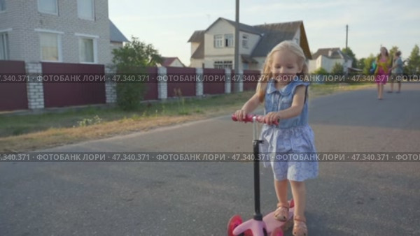 A little girl in the village rides a scooter. Стоковое видео, видеограф Mikhail Davidovich / Фотобанк Лори