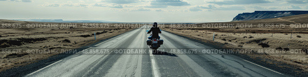 A lone motorcyclist rides down a straight, paved road through a barren, desert landscape. The sky is clear and blue, with a few fluffy clouds. Стоковое AI-изображение, AI-художник Данила Большаков / Фотобанк Лори