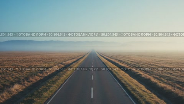 A long, straight road stretches through a vast, open landscape. The horizon is clear with a blue sky and distant mountains. Fog covers the ground, creating a serene atmosphere. Стоковое AI-видео, аниматор Olga Dmitrieva / Фотобанк Лори