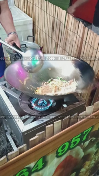 A man cooks a secret food Pad Thai in a wok on the street, tossing and turning the noodles and bean sprouts. Mobile vertical video. Thailand, Pattaya. Редакционное видео, видеограф Коханова Наталья / Фотобанк Лори