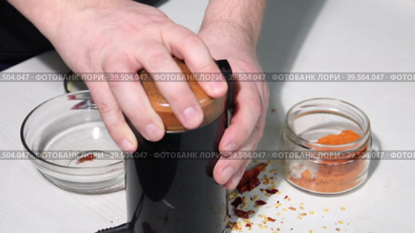 A man grinds dried red peppers in a coffee grinder. Shows the degree of grinding. Grinding hot pepper. Close-up. Стоковое видео, видеограф Vadzim Yakubovich / Фотобанк Лори