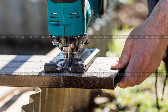 A man holds a battery-powered electric saw and builds new beds in a greenhouse made of wood-polymer composite. Macro photography. Side view. Preparing for the spring garden season. Стоковое фото, фотограф Photojuli / Фотобанк Лори