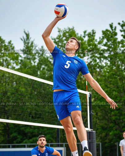 A man in a blue shirt and blue shorts is jumping to hit a volleyball. Стоковое AI-изображение, AI-художник Ярославский Максим / Фотобанк Лори