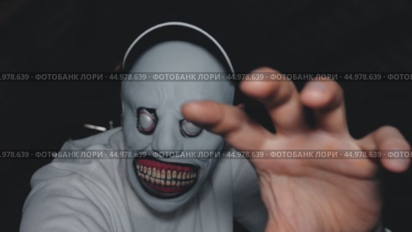 A man in a monster mask and white shirt holds out his hand. A black baseball cap is on his head. The monster lives in the attic. Стоковое видео, видеограф Воловодов Владимир / Фотобанк Лори