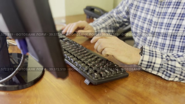 A man in a plaid shirt sits down at his desk in the office and starts typing on a computer keyboard. A sketch from the office. Стоковое видео, видеограф Ярославский Максим / Фотобанк Лори