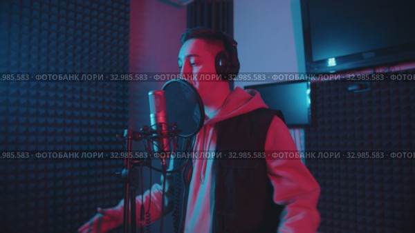 A man in headphones rapping in the studio gesticulates while recording his track - neon lighting. Стоковое видео, видеограф Константин Шишкин / Фотобанк Лори