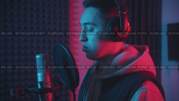A man in headphones rapping through the pop-filter in the microphone - studio in neon lighting. Стоковое видео, видеограф Константин Шишкин / Фотобанк Лори