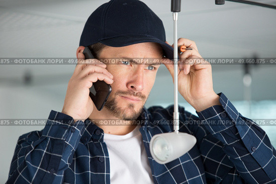 a man talking on the phone while fixing a light. Стоковое фото, агентство Ingram Publishing / Фотобанк Лори