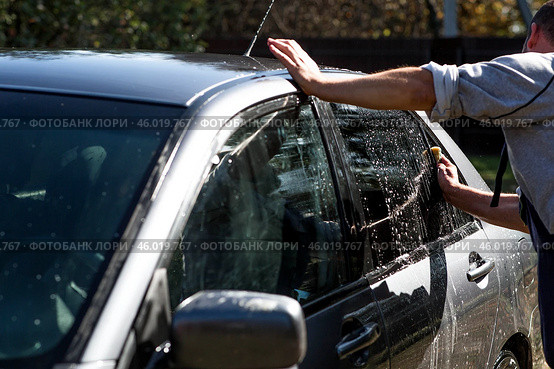 A man washes his car on the street of a suburban area. He hoses the car with water, washing away dirt and dust. Стоковое фото, фотограф Photojuli / Фотобанк Лори