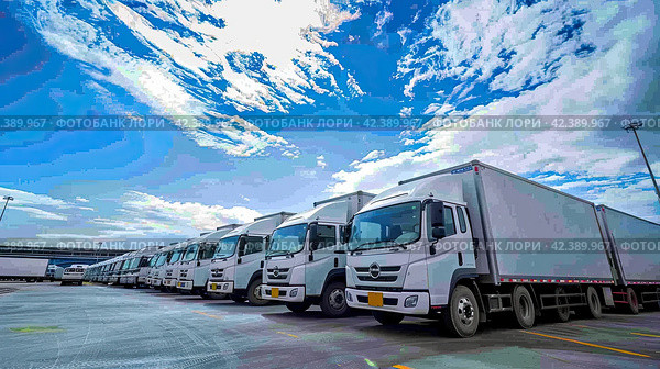 A parking lot for trucks with trailers, near the warehouse building, a background of blue sky. Cargo business. Generated by AI. Стоковое AI-изображение, AI-художник Ярославский Максим / Фотобанк Лори