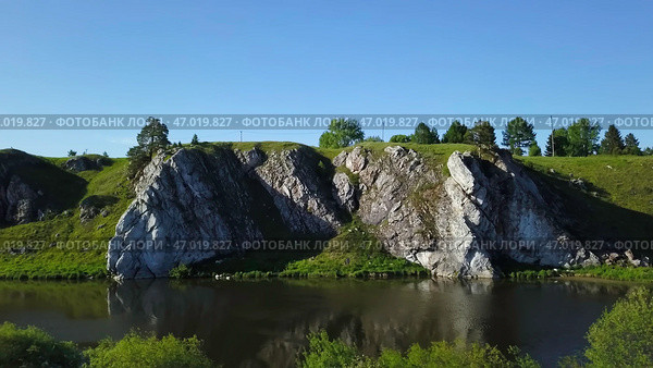 A picturesque scenic rock formation located near a tranquil river beneath a clear blue sky. Стоковое фото, фотограф David Kashakhi / Фотобанк Лори