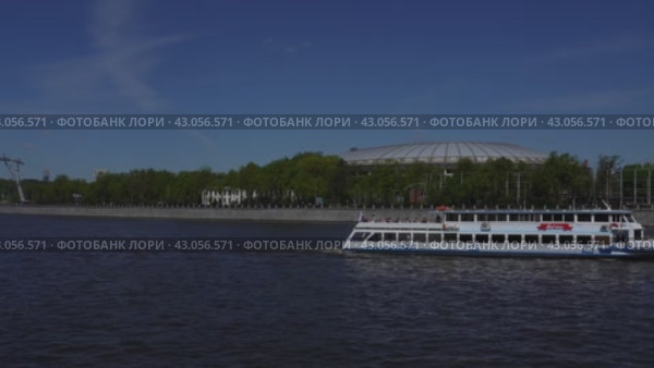 A pleasure boat passes along the Moscow River past a large sports arena. It's a sunny day. Russia. Moscow. 01.05.2024. Редакционное видео, видеограф Ярославский Максим / Фотобанк Лори